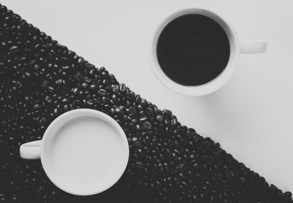 A table with a triangular parallel divide, one half black one half white. On black half a white cup with white liquid and on white half a white cup with black liquid - symbolising division